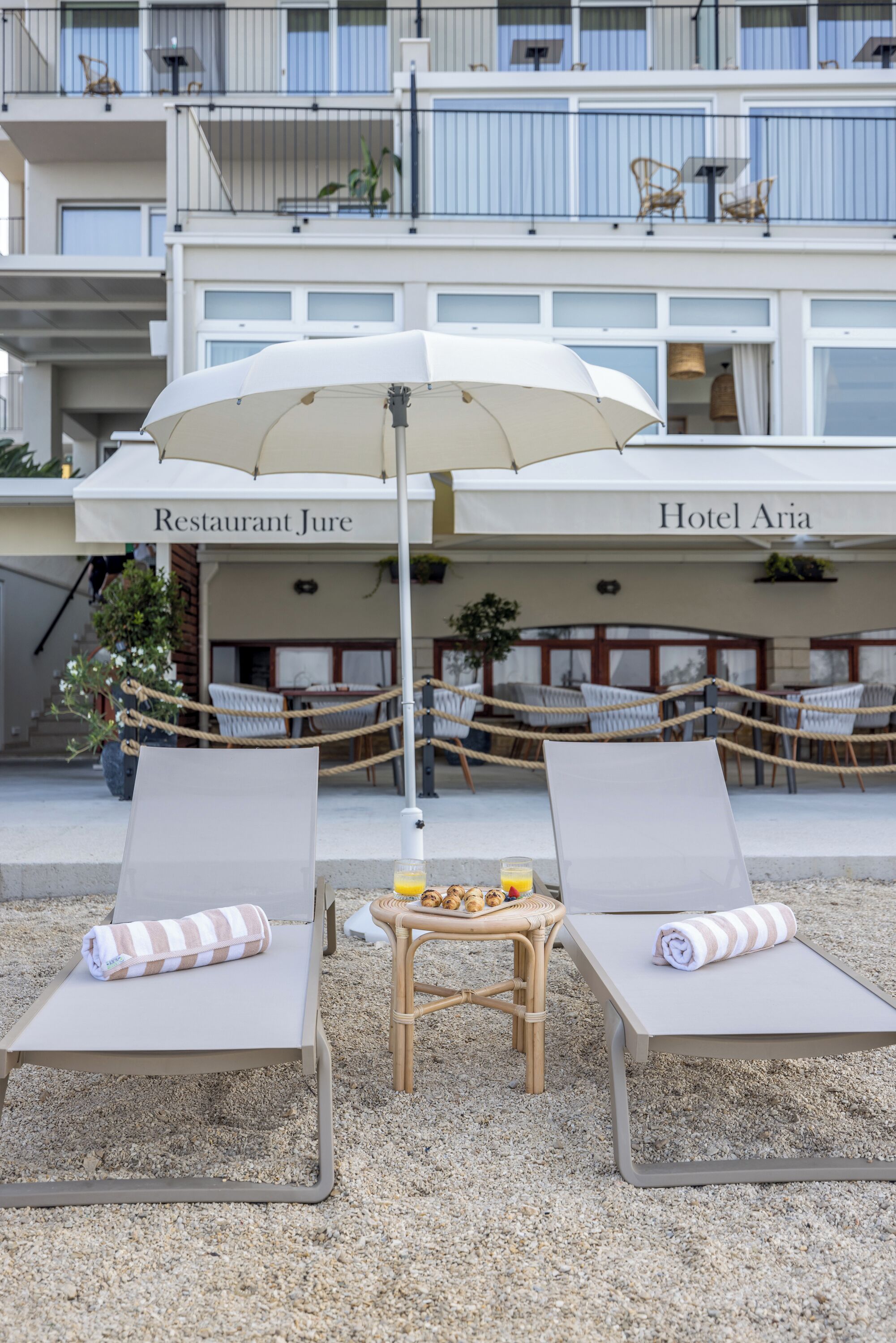 Zona relax in spiaggia con due lettini, un tavolo con un drink e un ombrellone grande.