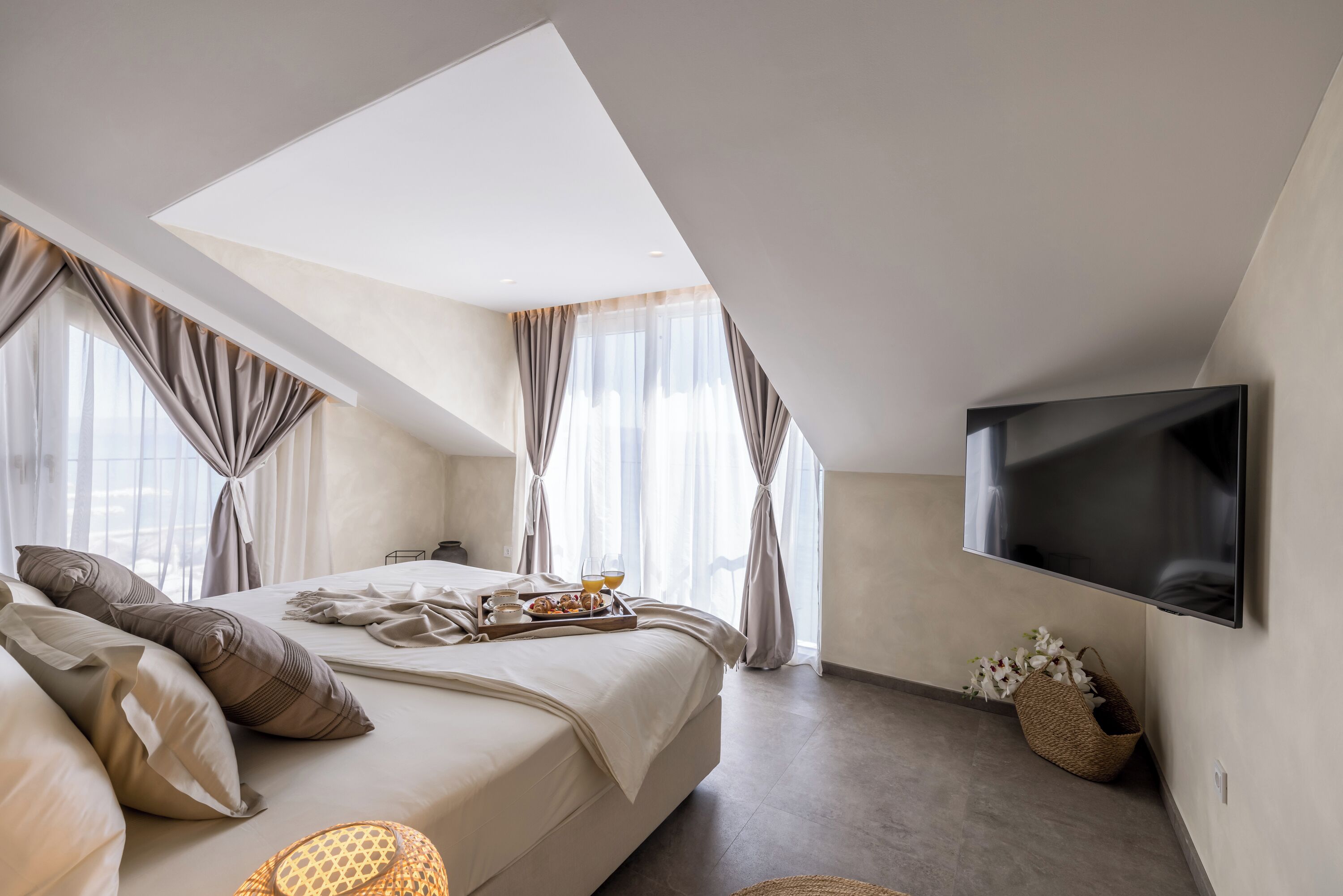 A modern bedroom with a large bed, a flat-screen TV, and a skylight.