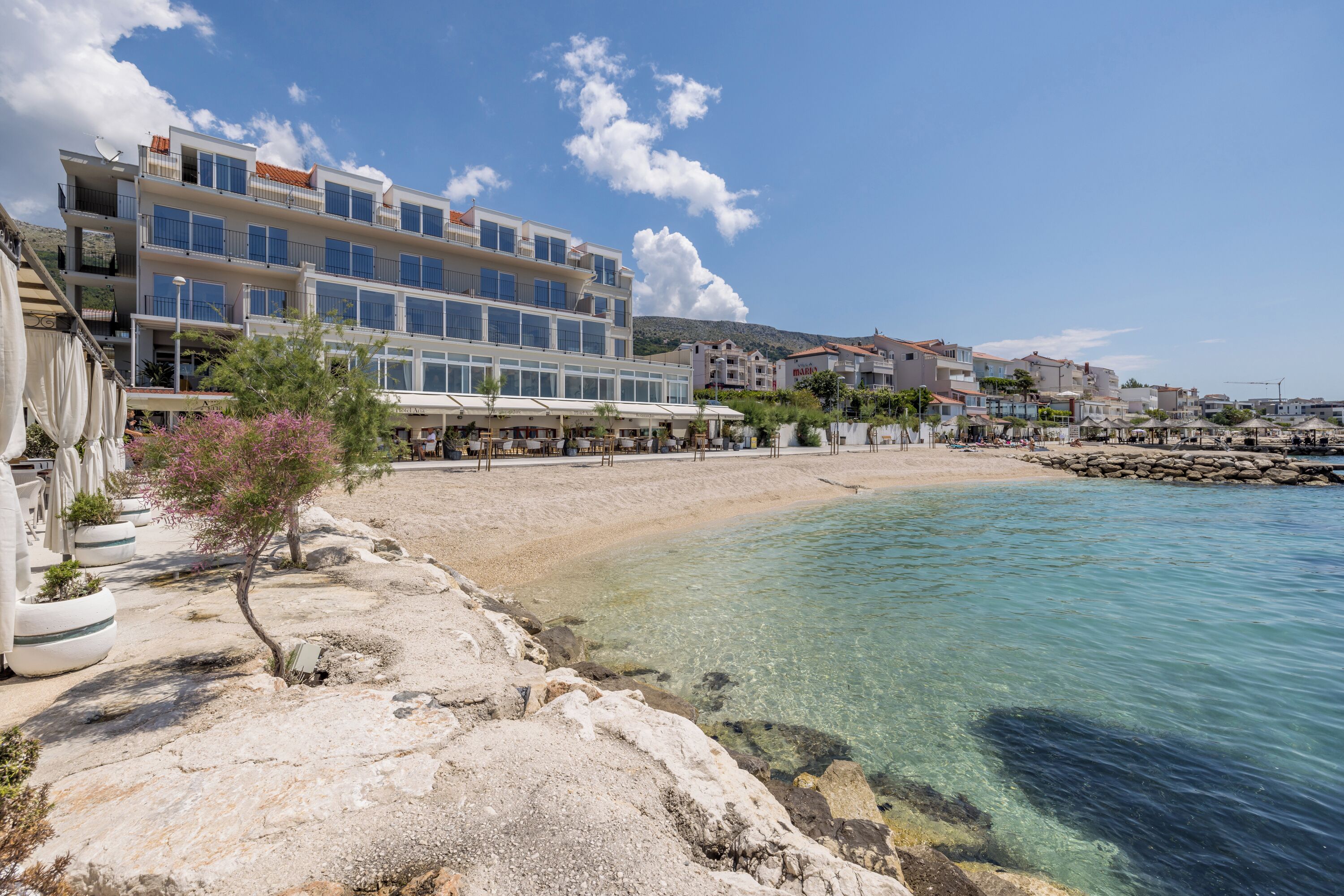 A coastal hotel with multiple floors, outdoor seating, and a clear view of the sea.