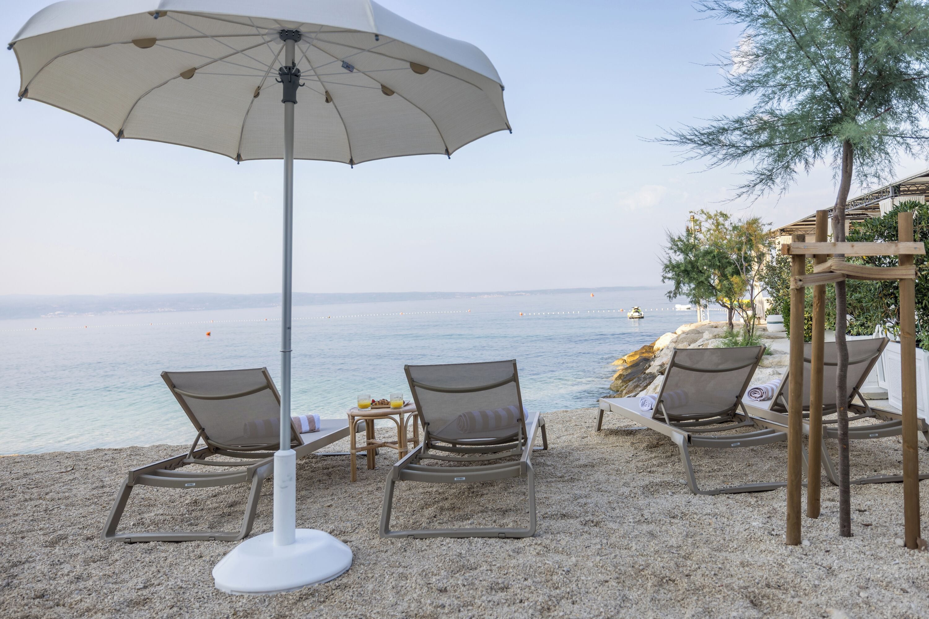 Eine Strandlounge mit Liegestühlen, einem großen Sonnenschirm und Blick auf das Meer.