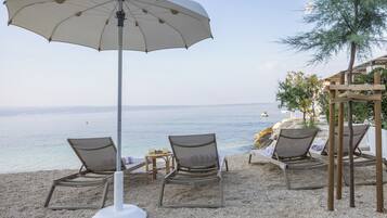 Eine Strandlounge mit Liegestühlen, einem großen Sonnenschirm und Blick auf das Meer.
