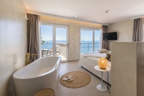 A modern bathroom with a freestanding bathtub, a round woven rug, and a bedside table with a lamp. - Hotel Aria (Podstrana)