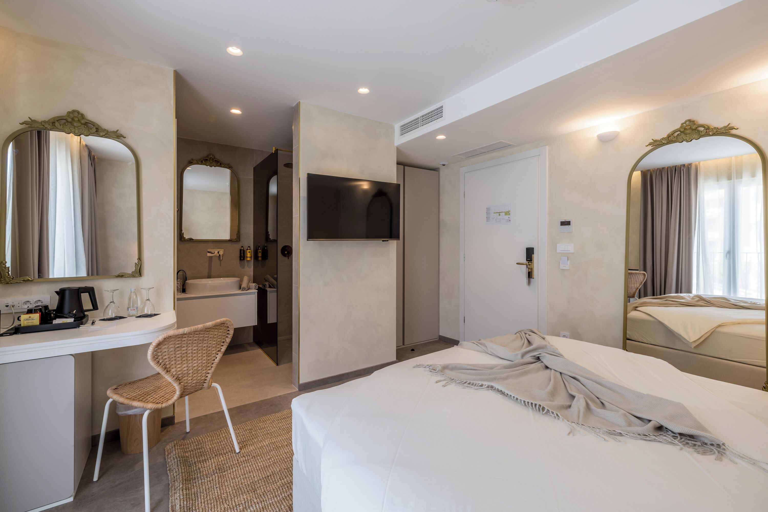Habitación de hotel con cama, escritorio con silla, televisor y baño con espejo y lavamanos.
