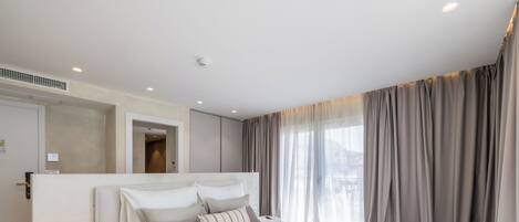Quarto de hotel moderno com uma cama grande, uma mesa de cabeceira com abajur e vista para a cidade através de grandes janelas.