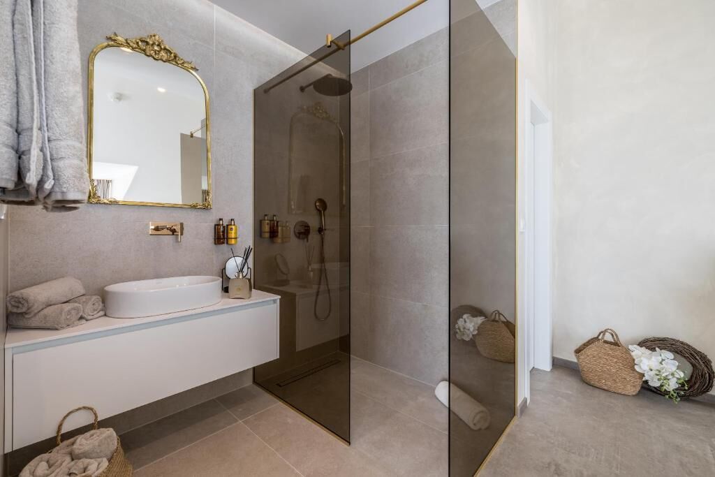Une salle de bain moderne avec une douche en verre, un lavabo blanc et un grand miroir doté d’un cadre orné.