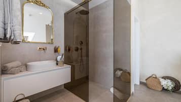 Un baño moderno con ducha de vidrio, un lavamanos blanco y un espejo grande con un marco decorativo.
