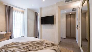 A modern hotel room with a large bed, a flat-screen TV mounted on the wall, a seating area with a chair, and a bathroom visible through an open door.