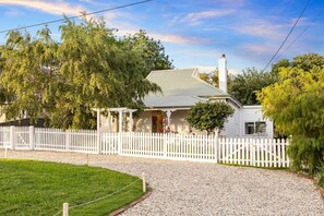 A house with a white picket fence, a gravel driveway, and a well-maintained lawn.