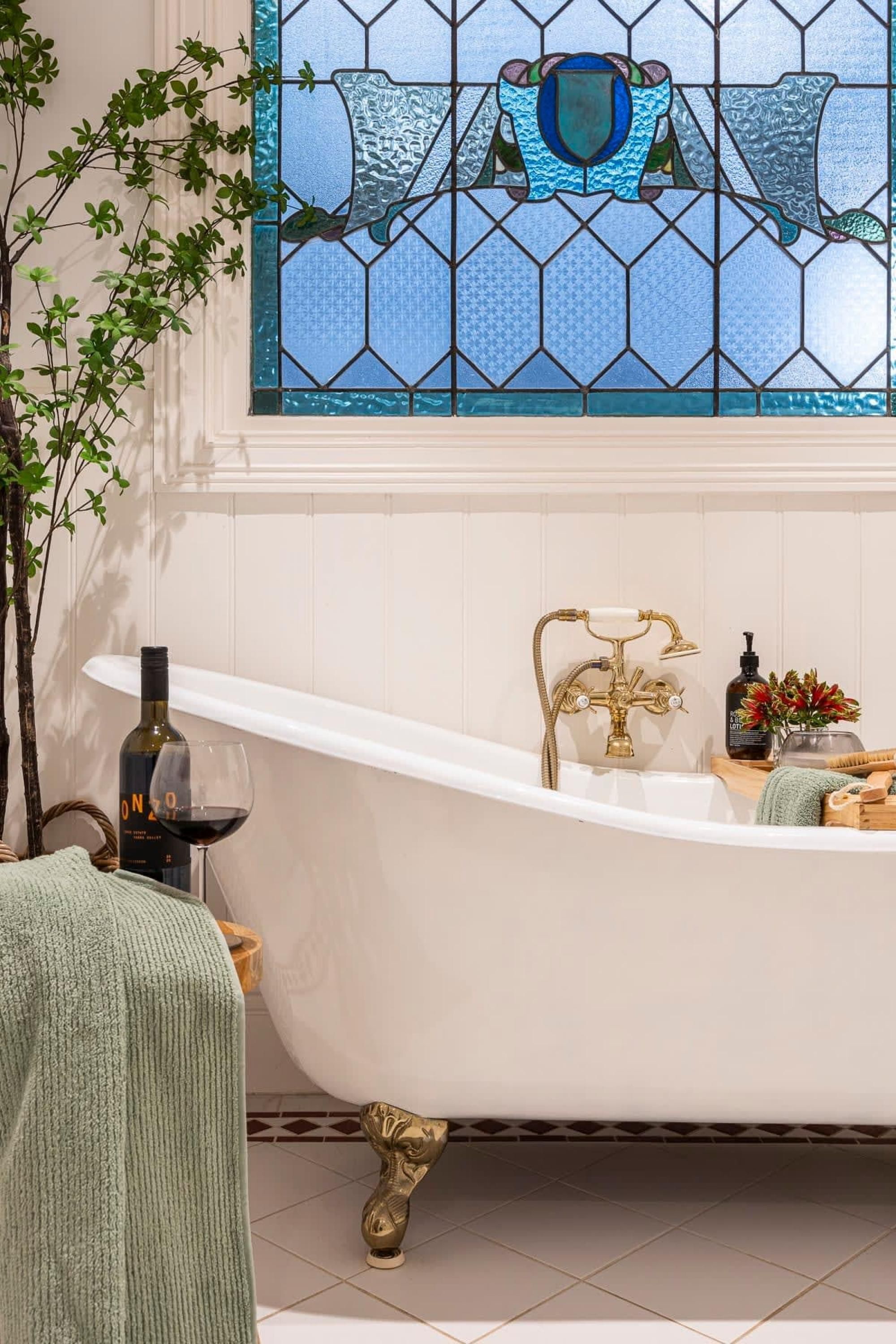 Ein Badezimmer mit einer freistehenden Badewanne, einem Messingarmaturen und einer Weinflasche auf einem Regal.