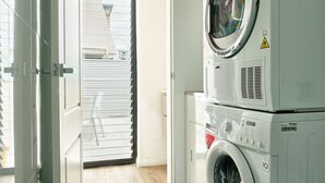 A laundry room with stacked washers and dryers, a door leading to an outdoor area, and a visible window. - Balmain Family Tranquility - Harbour Views (Balmain East)