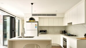 A modern kitchen with white cabinetry, a central island, a built-in oven, and a microwave. - Balmain Family Tranquility - Harbour Views (Balmain East)
