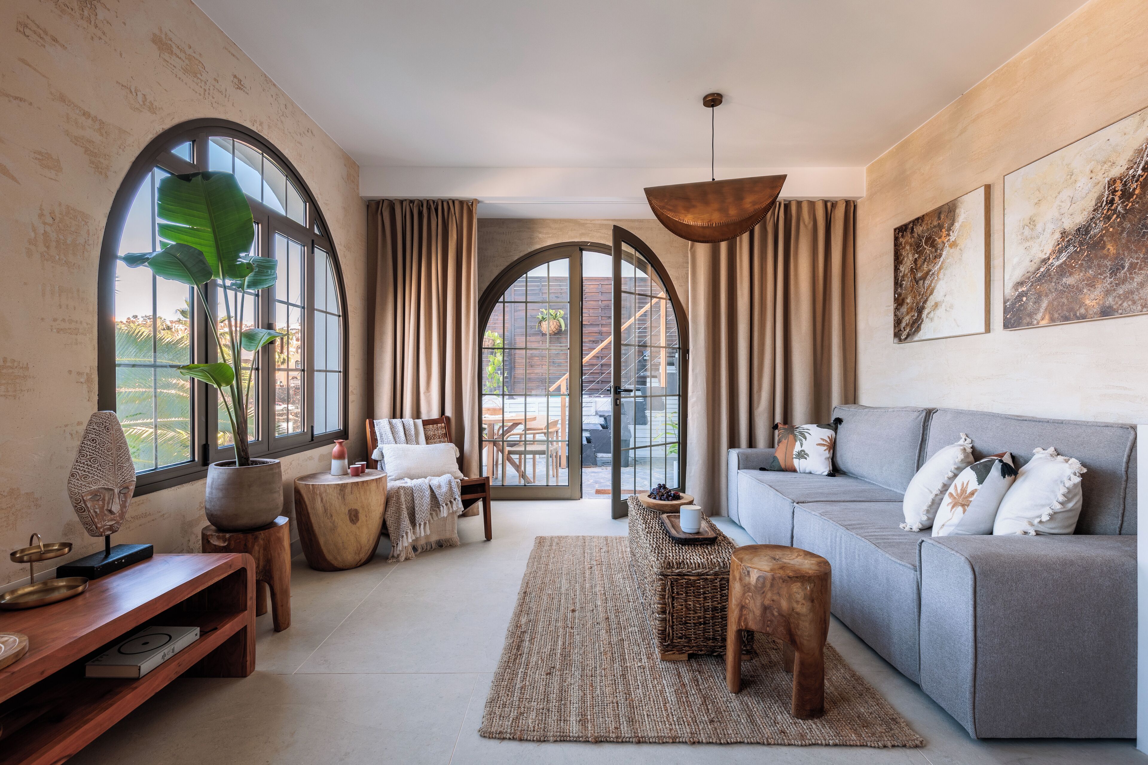 A spacious living room with a grey sofa, wooden coffee table, and a large plant.