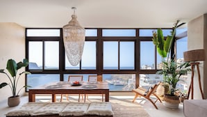 Un comedor con mesa de madera, sillas y un banco, con vistas panorámicas al mar a través de amplios ventanales.
