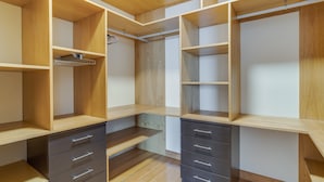 Un dressing avec des étagères en bois, un étendoir métallique et de nombreux tiroirs.