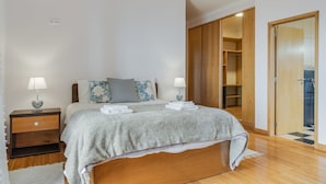 Une chambre à coucher comprenant un lit, des tables de chevet, une armoire et une salle de bain visible à travers une porte ouverte.