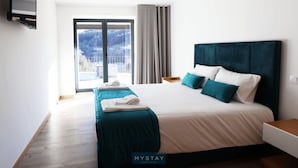 Ein modernes Hotelzimmer mit einem großen Bett, einem an der Wand montierten Fernseher, einem Balkon mit Blick auf die Stadt und einem Holzboden.