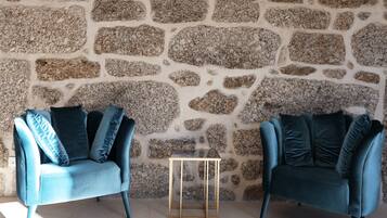 Two blue armchairs with cushions against a stone wall.