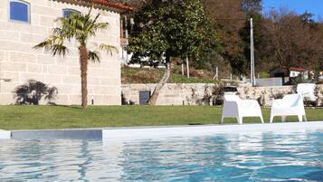 A swimming pool with white lounge chairs, a stone building with windows, and a palm tree.