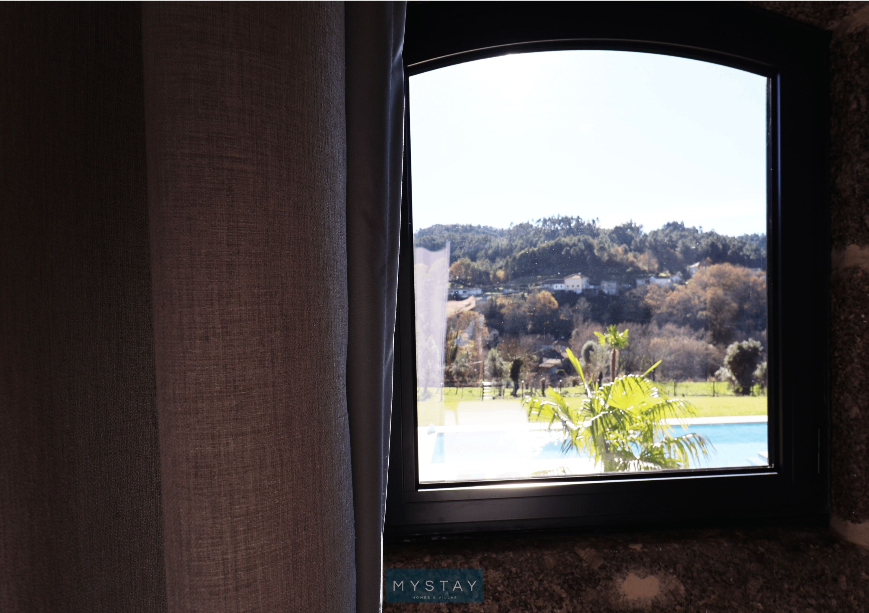 A window with a view of a pool and a hilly landscape.