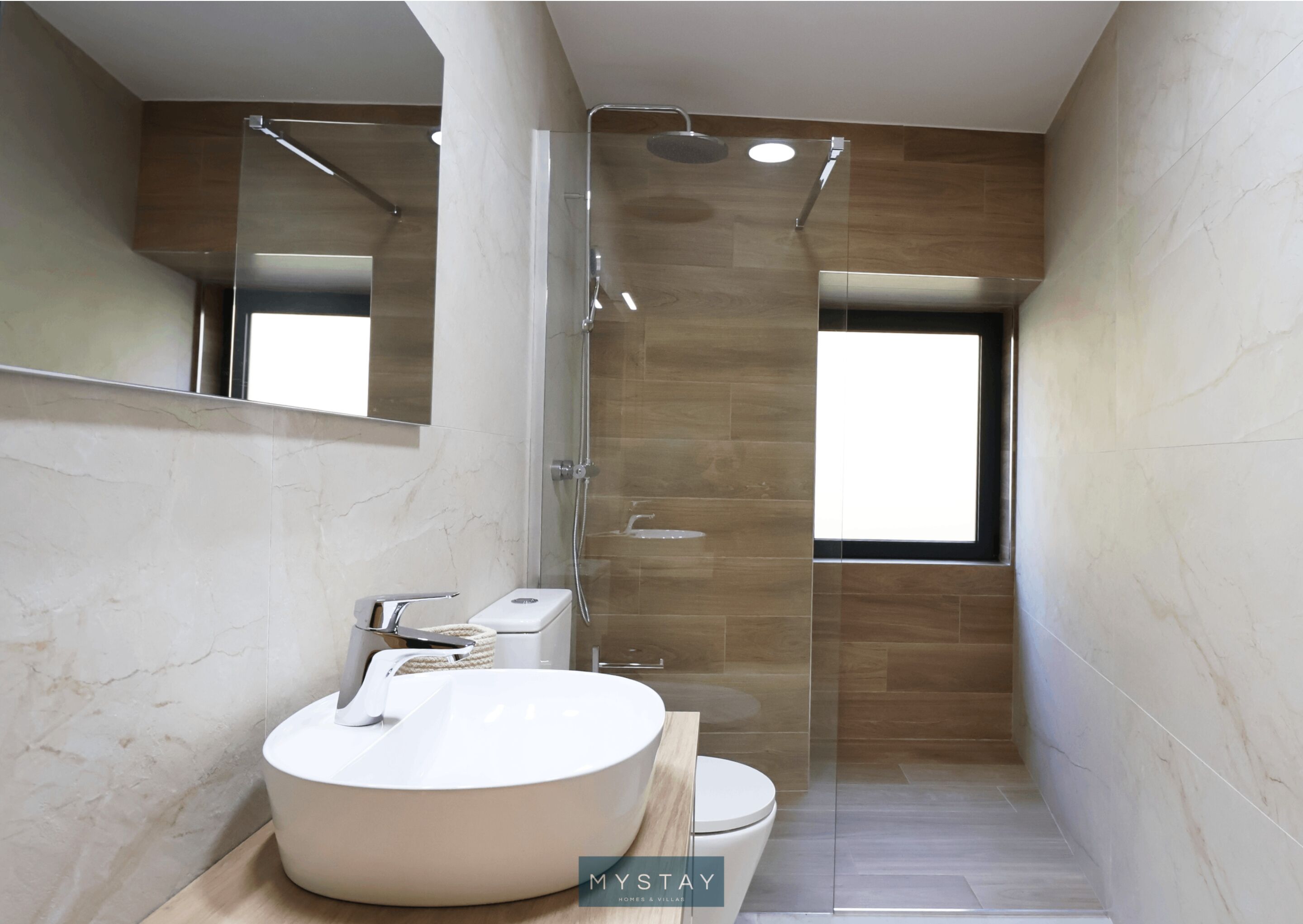 Un baño moderno con un lavamanos grande y blanco, un inodoro y una ducha con mampara de vidrio.