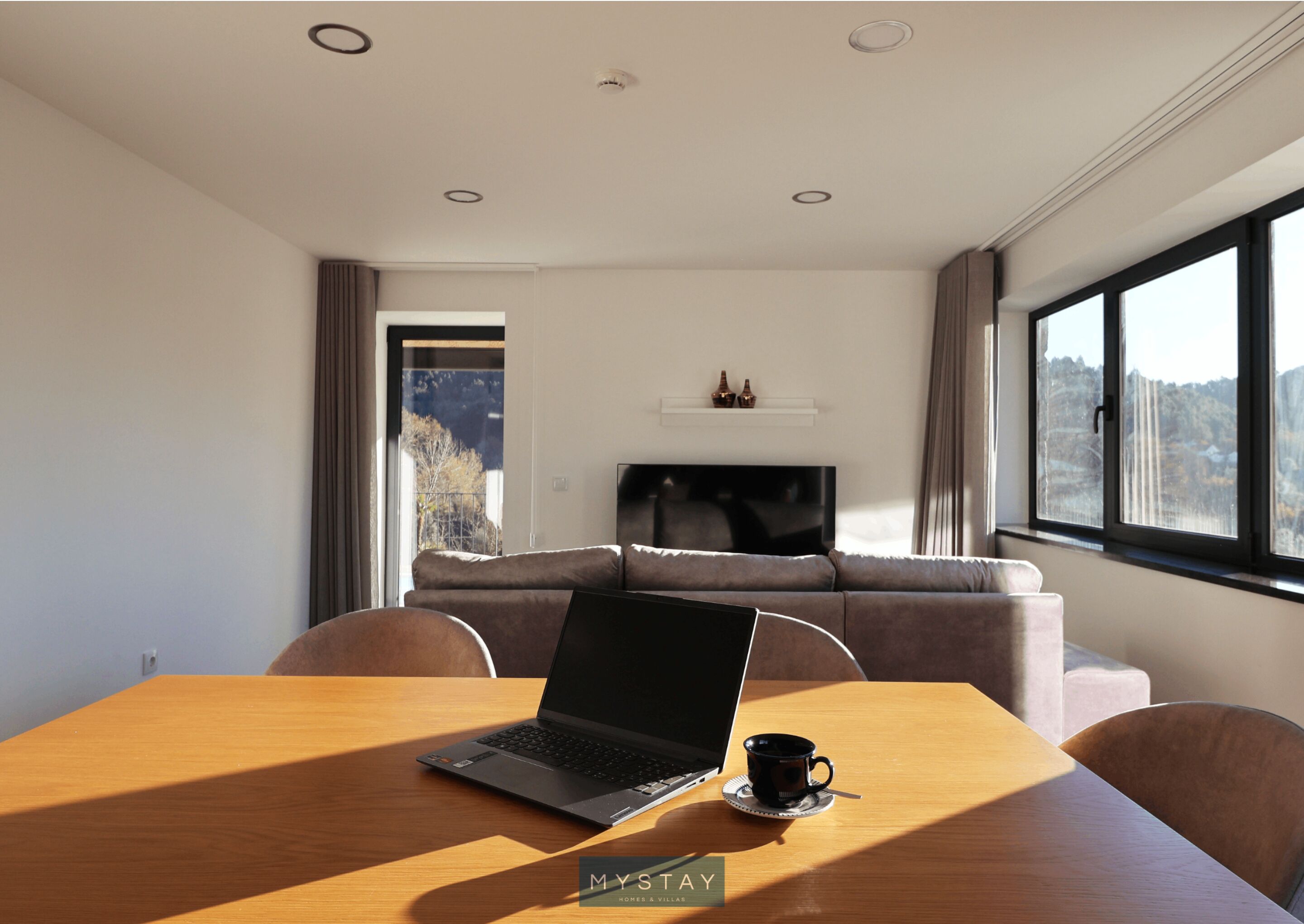 A modern room with a laptop on a wooden table, a sofa, and a TV.