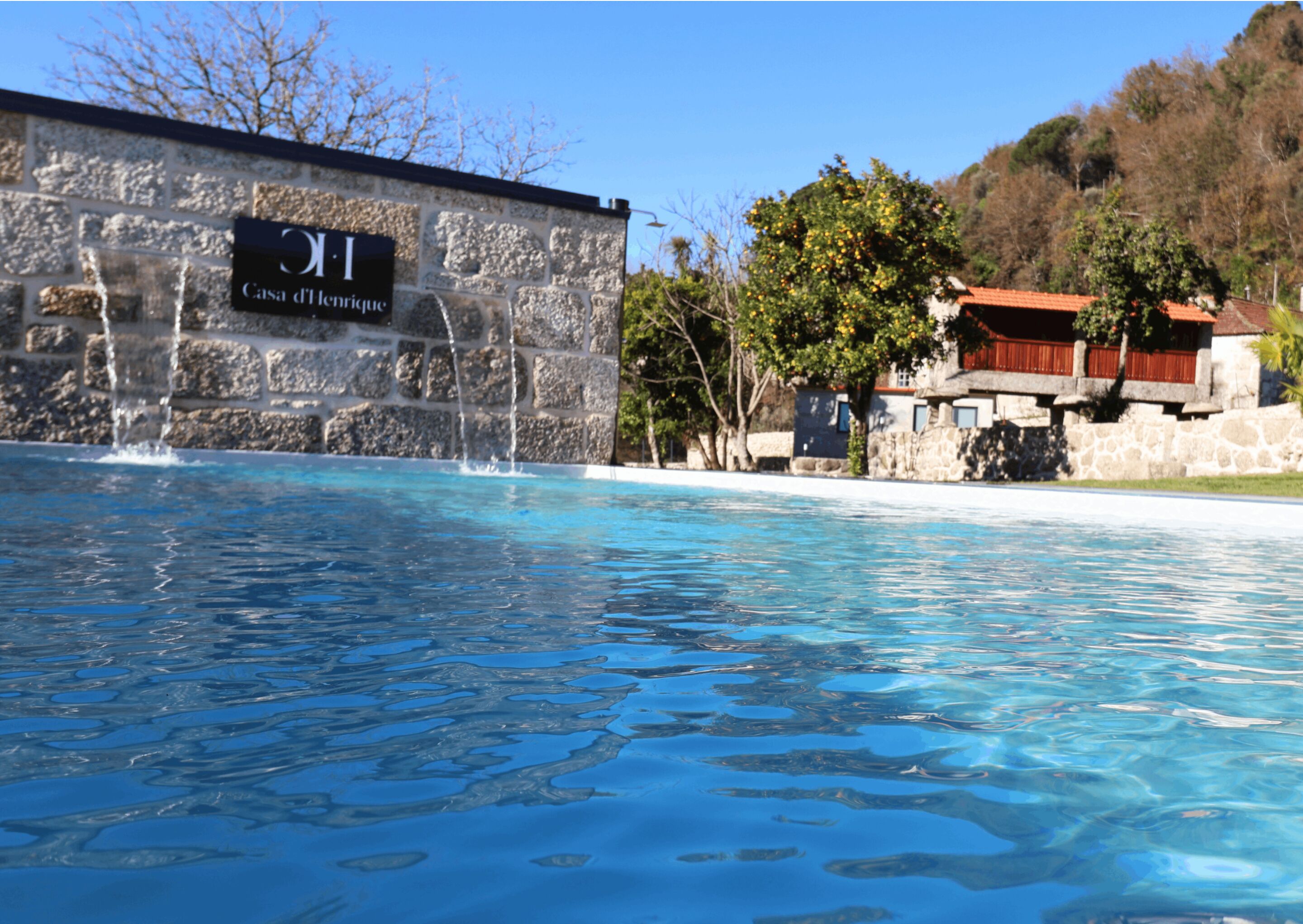 A swimming pool with a stone wall and a sign reading "Casa d'Enrique."