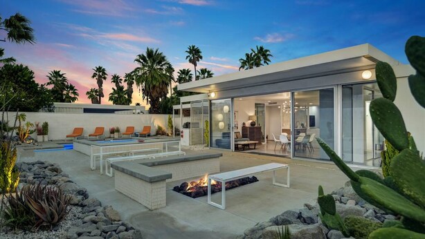 Ein moderner Außenbereich mit Pool, Liegestühlen, Feuerstelle und einem glasgeschlossenen Essbereich.