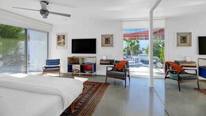Ein modernes Hotelzimmer mit einem großen Bett, einem Deckenventilator, einem Fernseher und Blick ins Freie.
