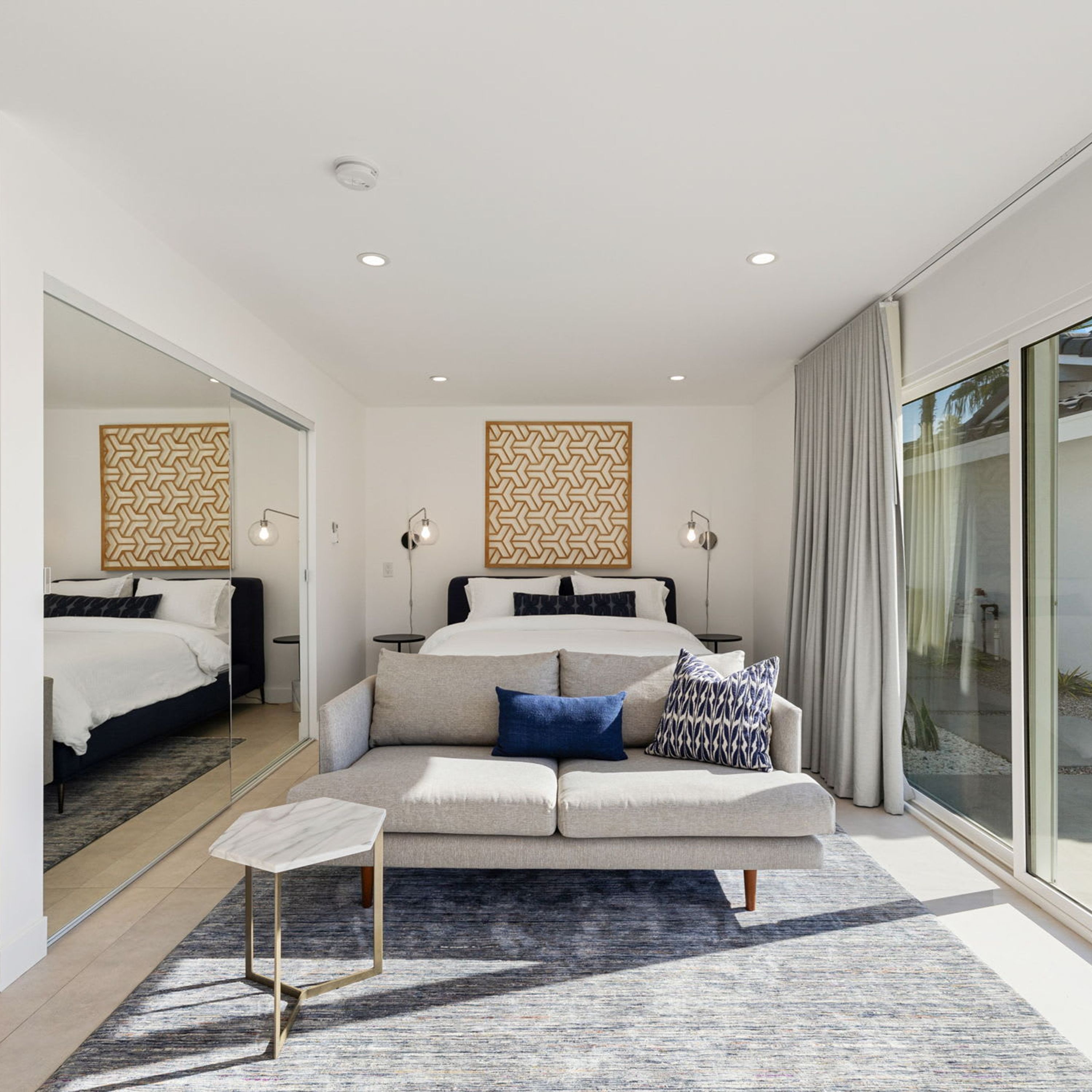 Et moderne hotelværelse med en stor seng, en sofa og et lille bord. Der er to væglamper og en loftlampe.