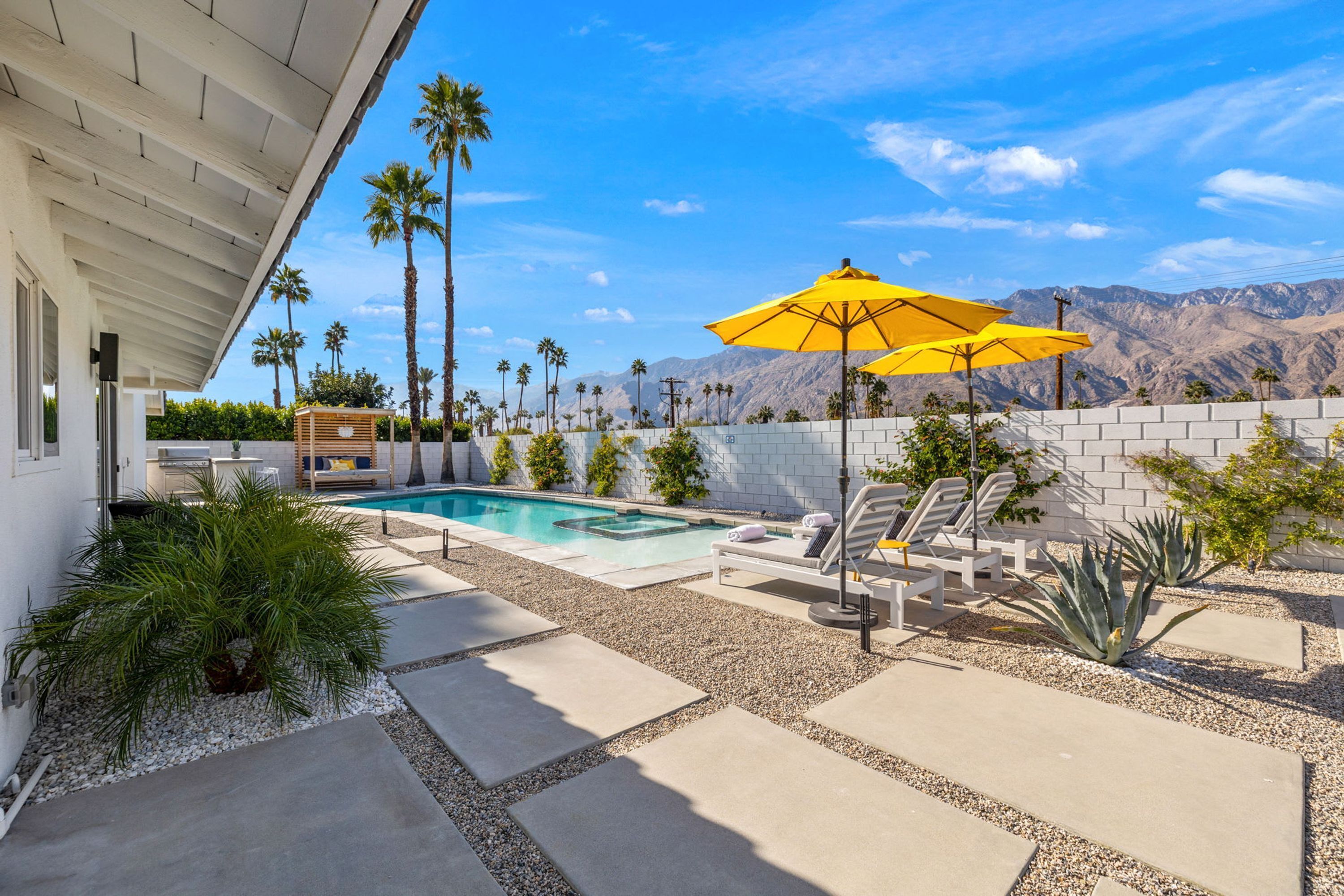 A pool area with a white wall, palm trees, and a mountain view.