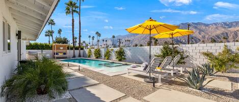 A pool area with a white wall, palm trees, and a mountain view.