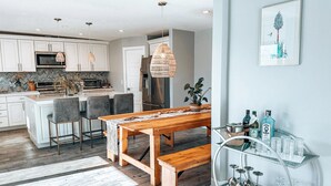A modern kitchen with white cabinets, a wooden dining table, and a bar cart with glasses and bottles. - The Yucca Hotel- Entire Boutique Buyout (Desert Hot Springs)