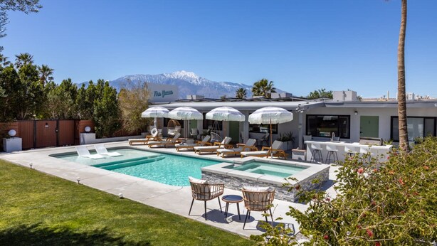 A pool area with lounge chairs and umbrellas, a dining area with bar stools, and a mountain view in the background. - The Yucca Hotel- Entire Boutique Buyout (Desert Hot Springs)