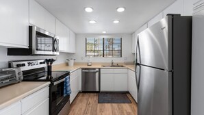 Una cocina moderna con armarios blancos, electrodomésticos de acero inoxidable, un ventanal con persianas y una alfombra negra.