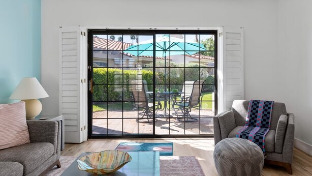 Una sala de estar con sofá, reposapiés, mesa de centro y vista a un patio exterior con mesa y sillas.