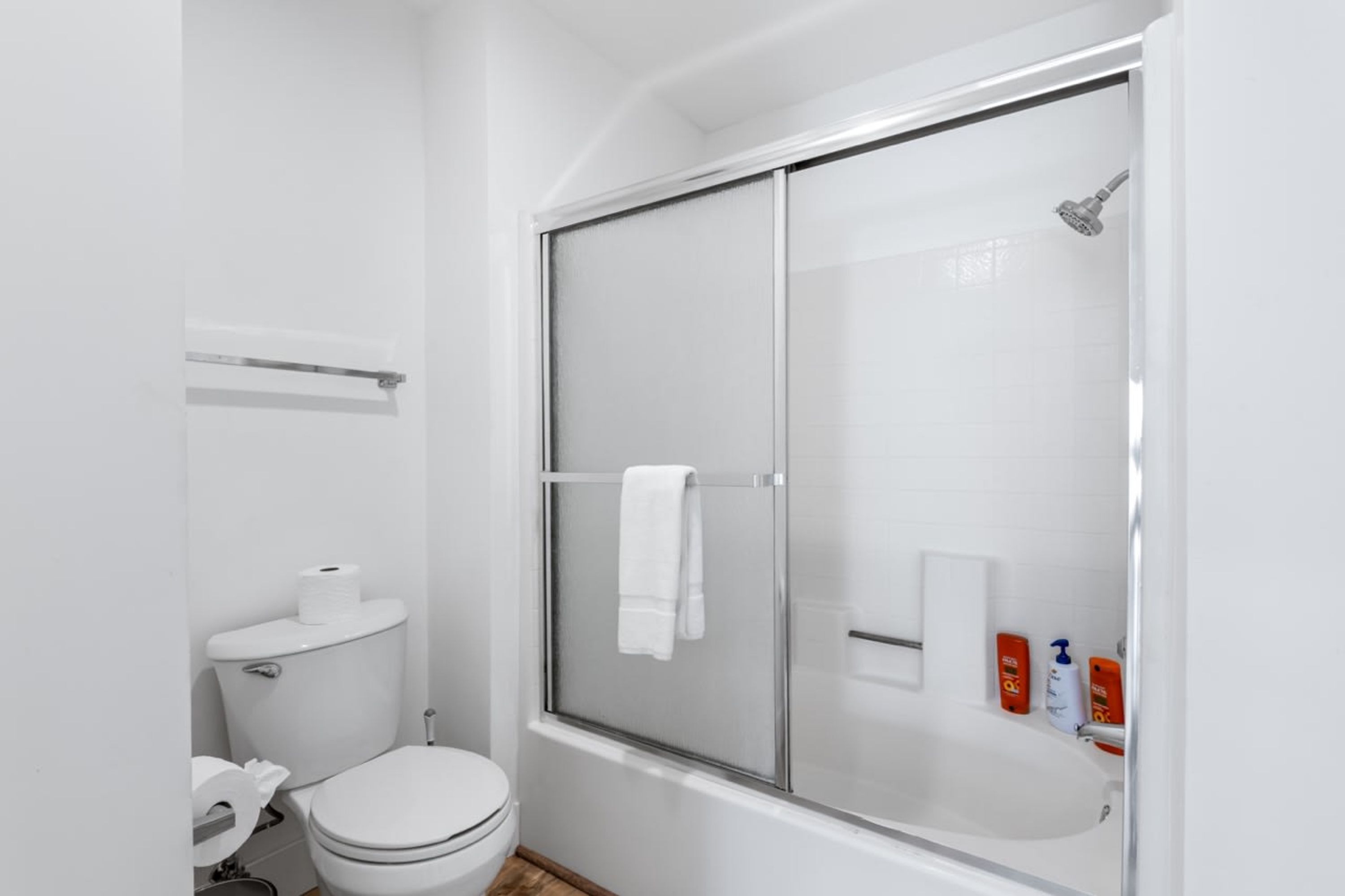 A bathroom with a toilet, a shower with a glass door, and toiletries on the wall.