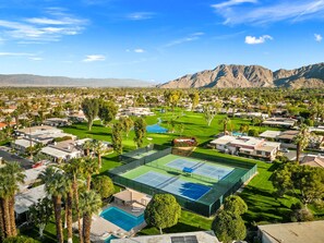 Zona residencial con una gran cancha de tenis, piscina y abundante vegetación.