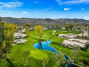Un campo de golf con piscina, rodeado de edificios residenciales y montañas al fondo.