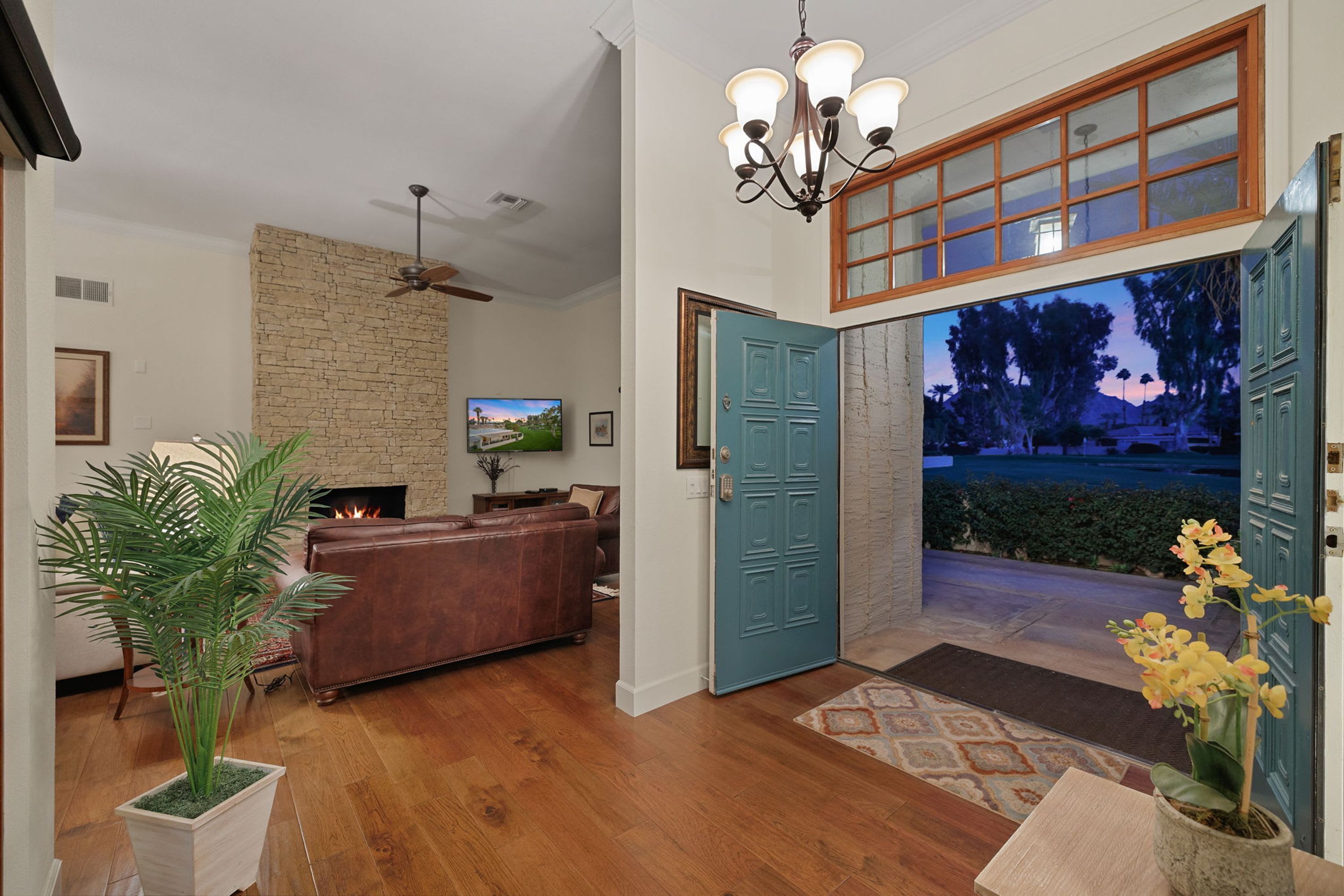A living room with a fireplace, a television, and a door leading to a balcony with a view of trees.