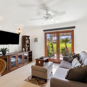 Relax in this stylish living room with a large flat-screen TV, comfortable sofa, and sliding glass door leading to a lush outdoor area.