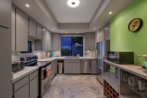 Une cuisine moderne dotée d’appareils électroménagers en acier inoxydable, d’une grande fenêtre et d’un mur d’accent de couleur verte.