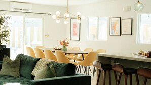 Ein modernes Wohnzimmer mit einem grünen Sofa, gelben Sesseln, einem Esstisch und einer Küchenzeile mit Barhocker.