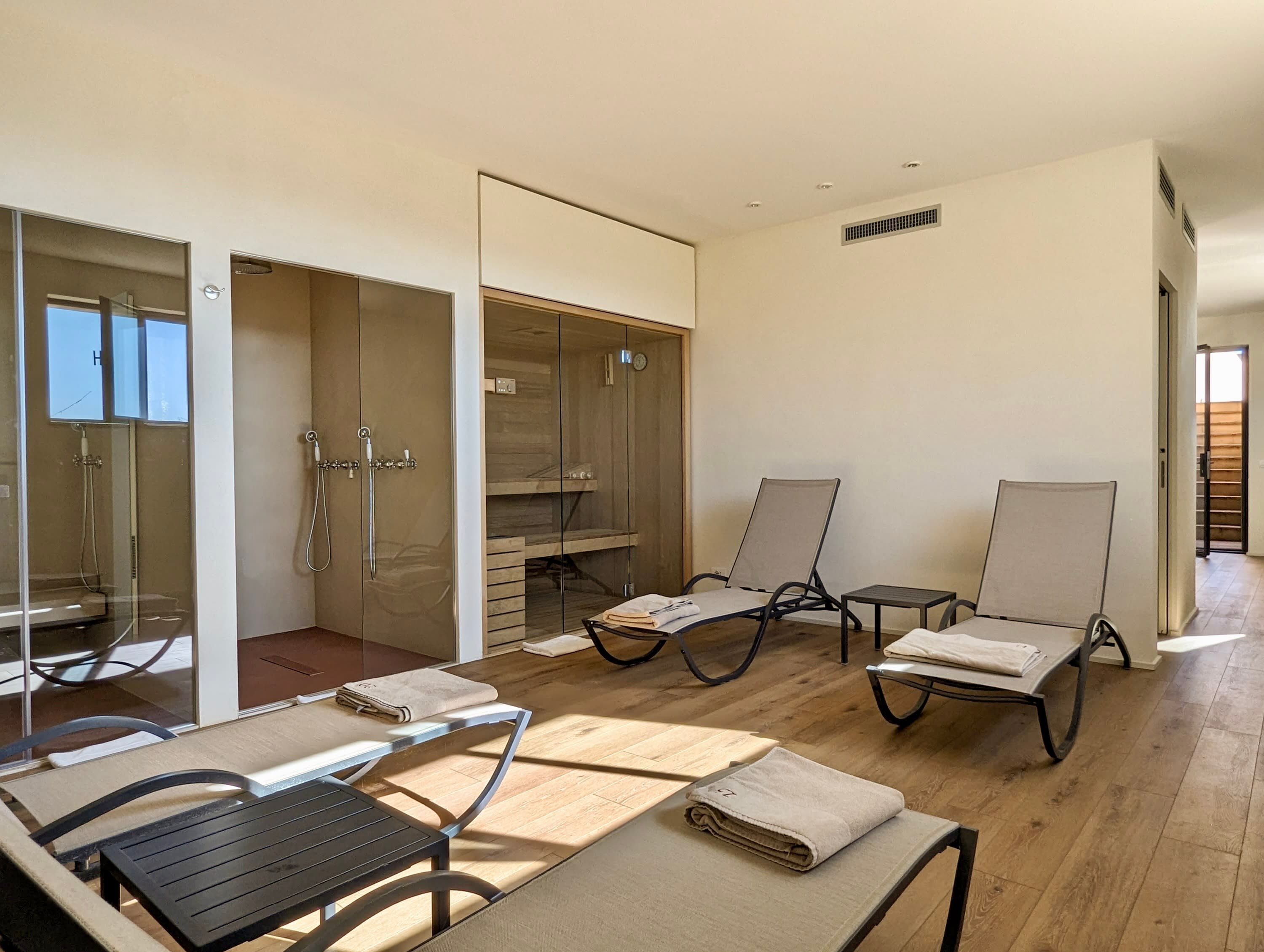 Ein moderner Wellnessraum mit einer gläsernen Dusche, zwei Liegestühlen und Holzboden.