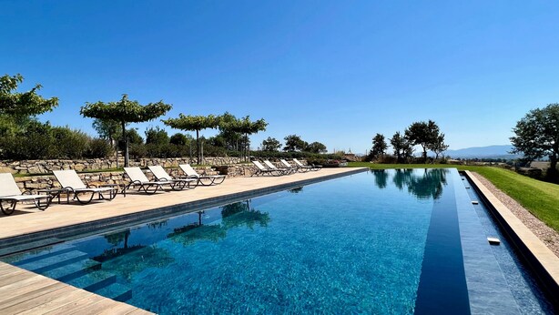 Una piscina infinita de color azul claro con sillones de descanso y una pared de piedra.