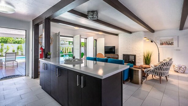 A modern kitchen with dark cabinetry, a central island, and a dining area with blue seating. - Mountain View Mid-century (Palm Springs)