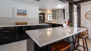 A modern kitchen with a large island, dark cabinetry, and a white backsplash. - Mountain View Mid-century (Palm Springs)