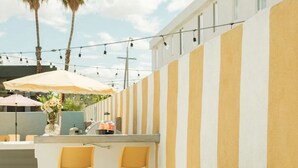 An outdoor seating area with a striped wall, two wooden chairs, a green sofa, and an umbrella. - Mod Hotel in Palm Springs (Palm Springs)