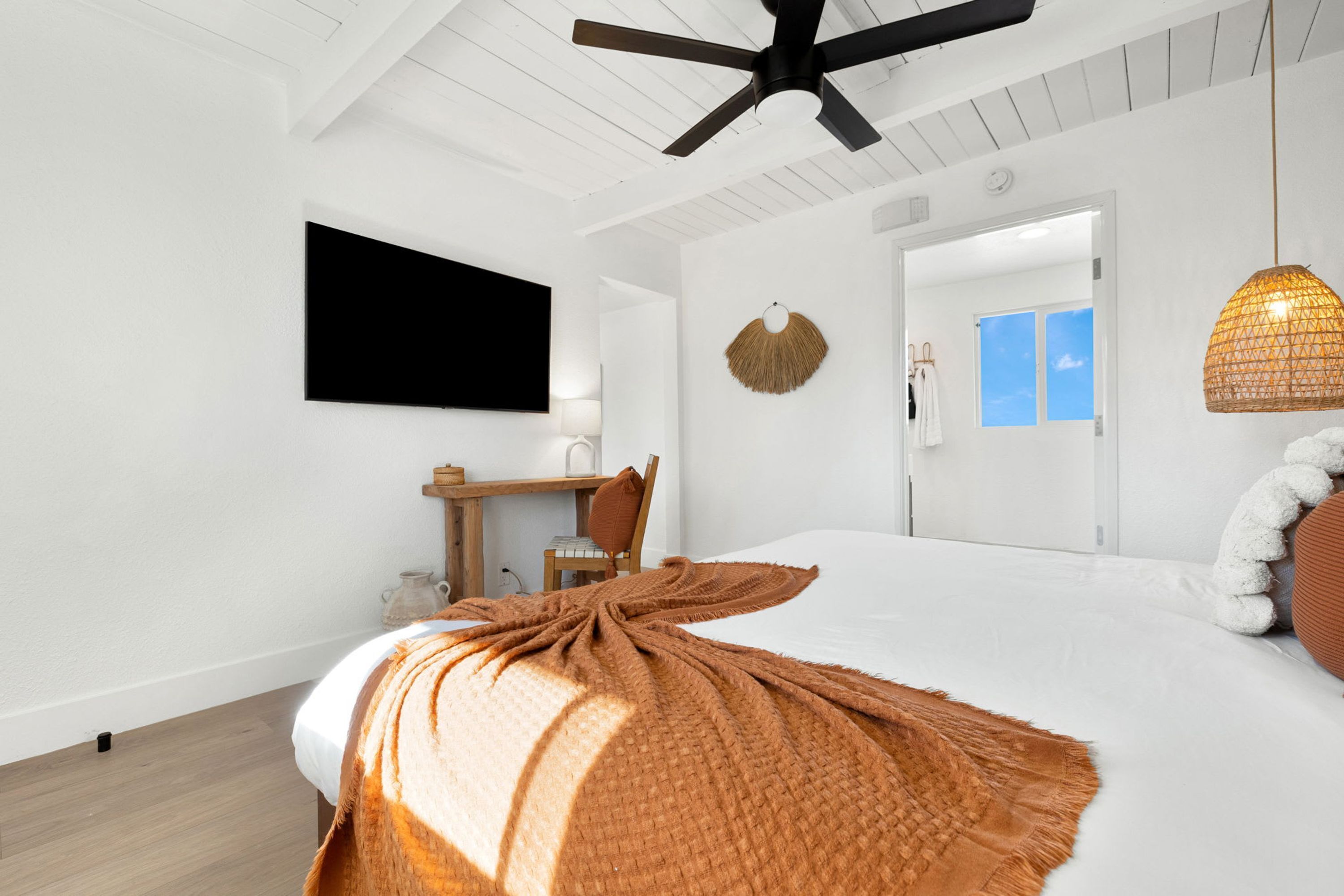 Un dormitorio moderno con una cama grande, un ventilador de techo, un televisor de pantalla plana y un escritorio con una silla.