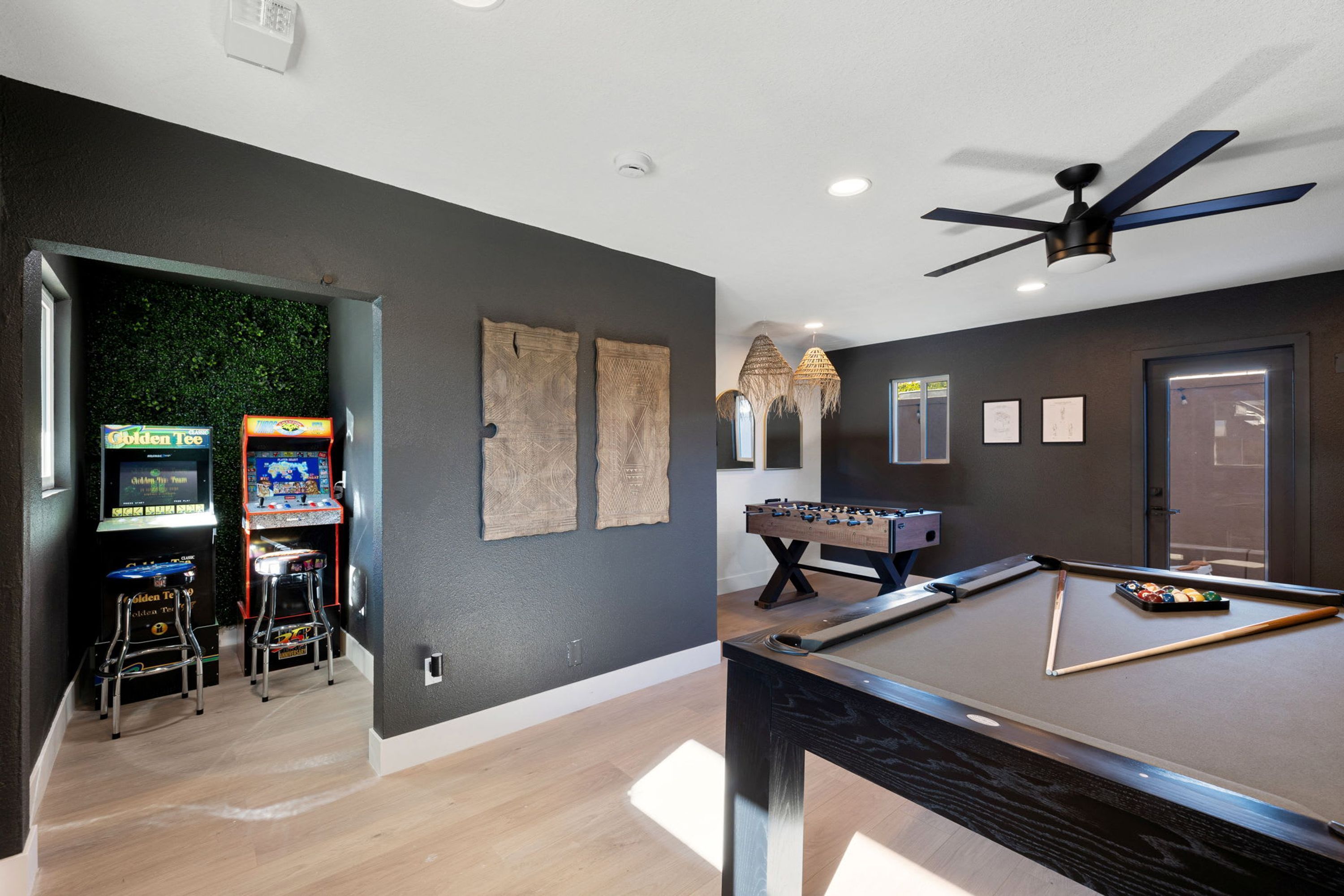 A room with a pool table, foosball table, and two arcade machines.