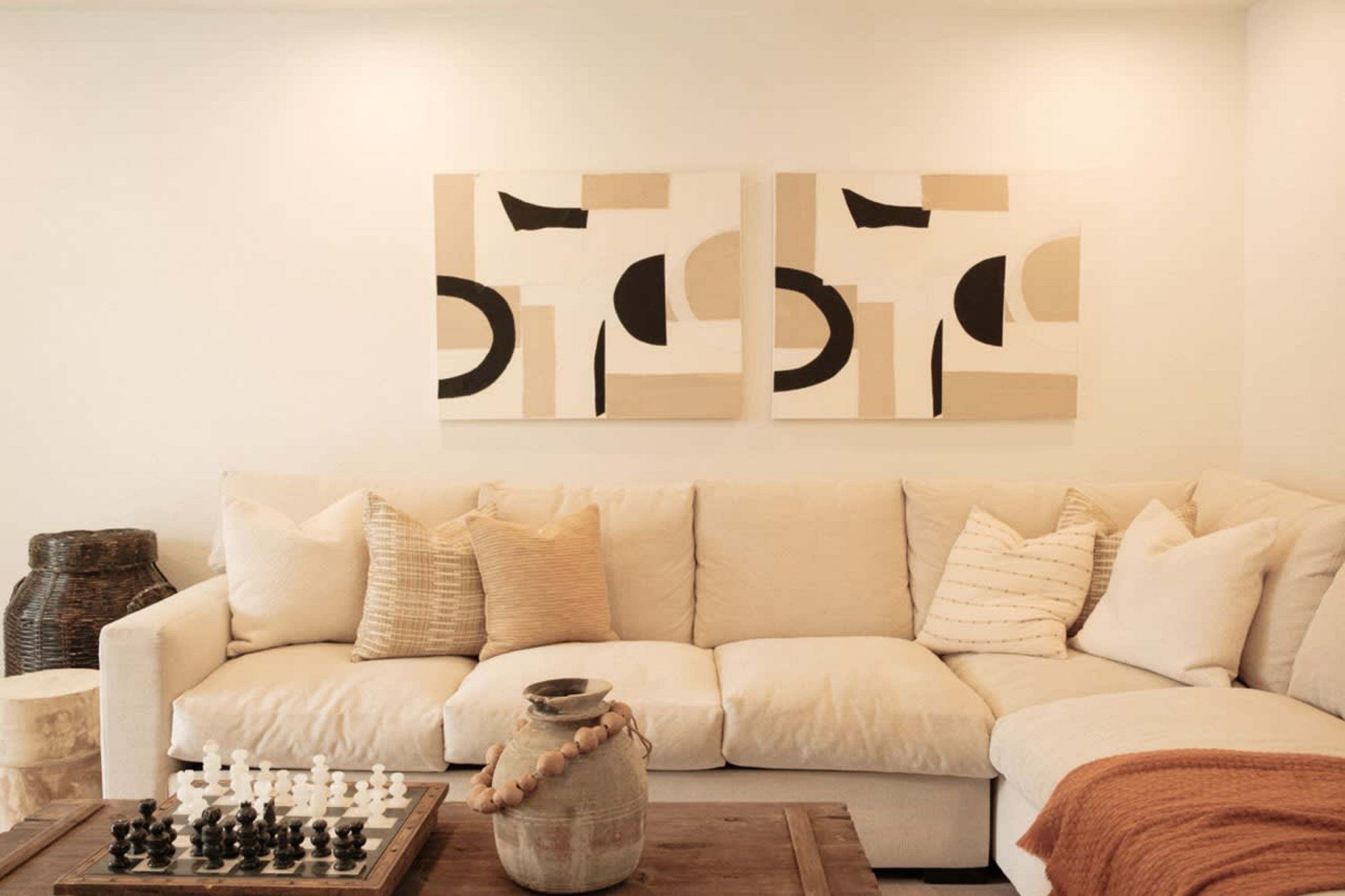 A living room with a beige sofa, a chessboard, and a vase on a wooden coffee table.